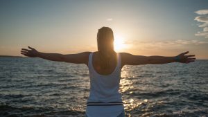 A woman stands with open arms, embracing the sunset over the ocean. San Juan Bautista, Spain.
